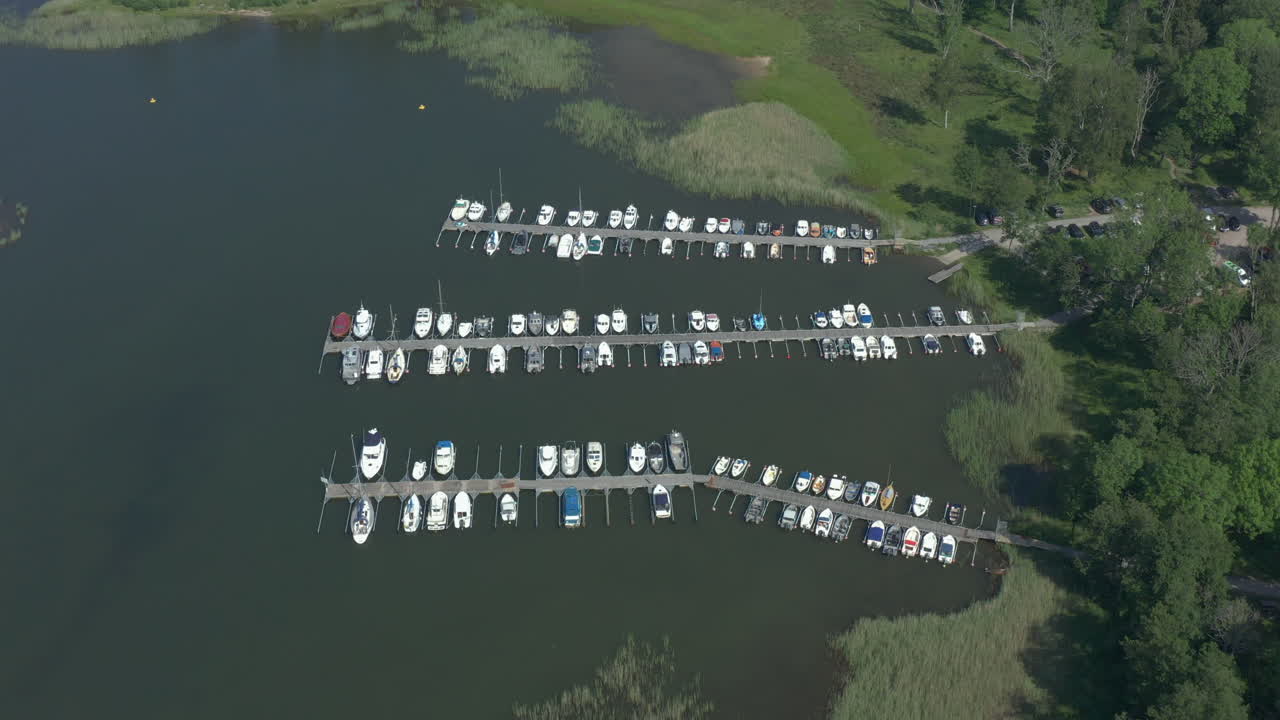 Boats docked at small remote harbor in scenic forest landscape, tilt down aerial