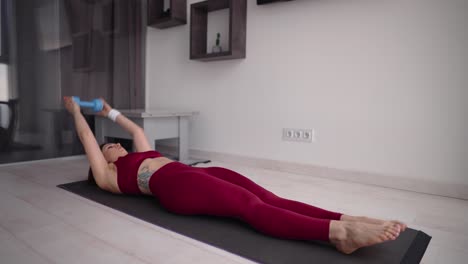 mujer haciendo ejercicio abdominal con pesas en sus manos en una alfombra en el suelo en la sala de estar