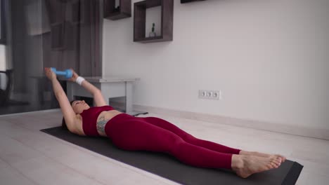 woman doing abdominal exercise with dumbbells in her hands on a mat on the floor in the living room