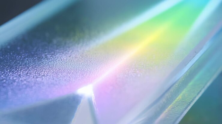 Un'ampia banda spettrale scorre lungo un bordo lucido e un piano curvo, passando da un punto luce brillante a un'ampia iridescenza arcobaleno, mentre una superficie texturizzata vicina mantiene una grana sottile, contrasto e profondità.