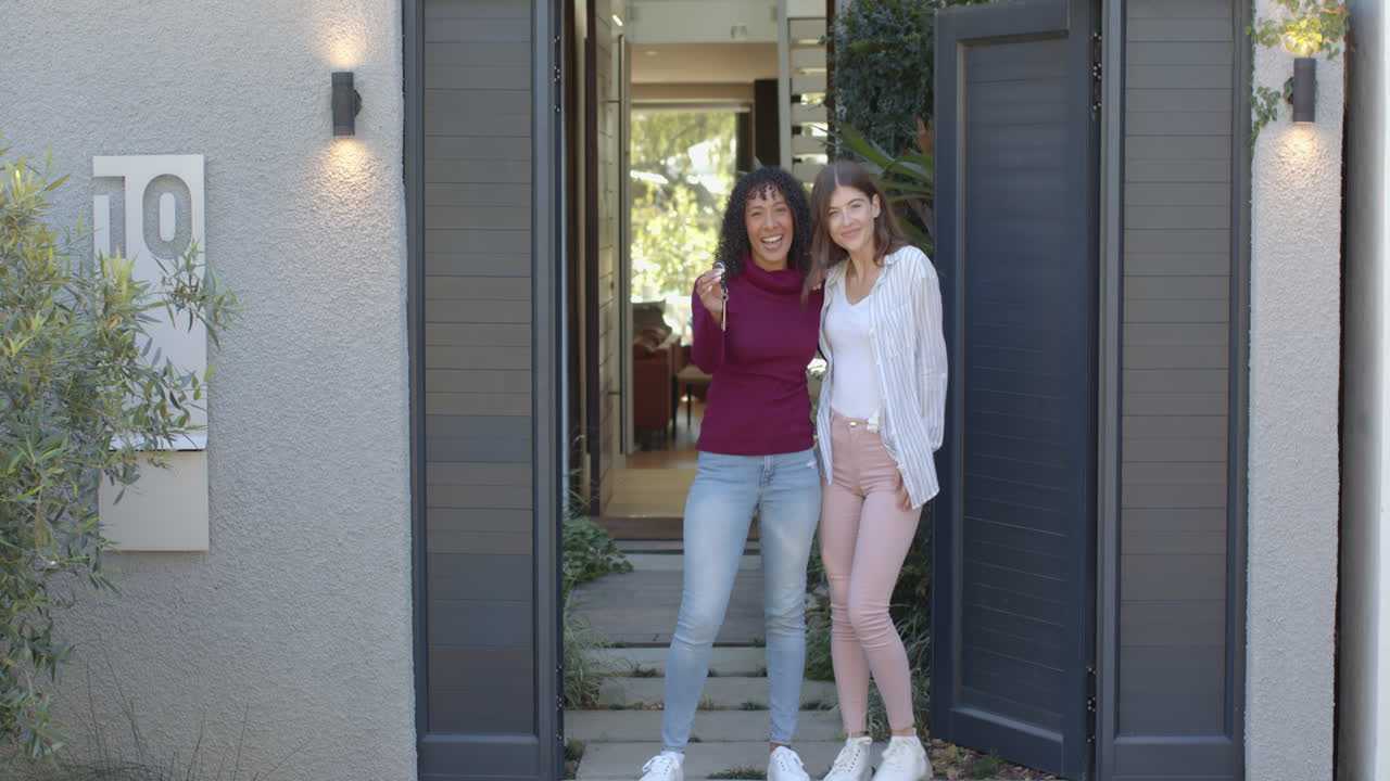 Standing at entrance, lesbian couple smiling and embracing outside their home
