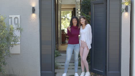 standing at entrance, lesbian couple smiling and embracing outside their home