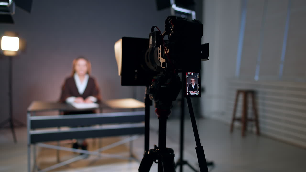 Camera set on tripod filming a woman sitting at desk. Female photographer stands up to fix the camera. Blogging concept.