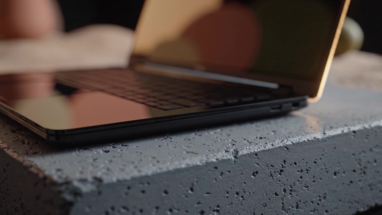 Viste Ravvicinate di un Laptop Moderno Appoggiato su una Superficie di Cemento Texturizzata, che Mostra una Fusione di Tecnologia e Design Minimalista in un Ambiente con Illuminazione Soffusa.