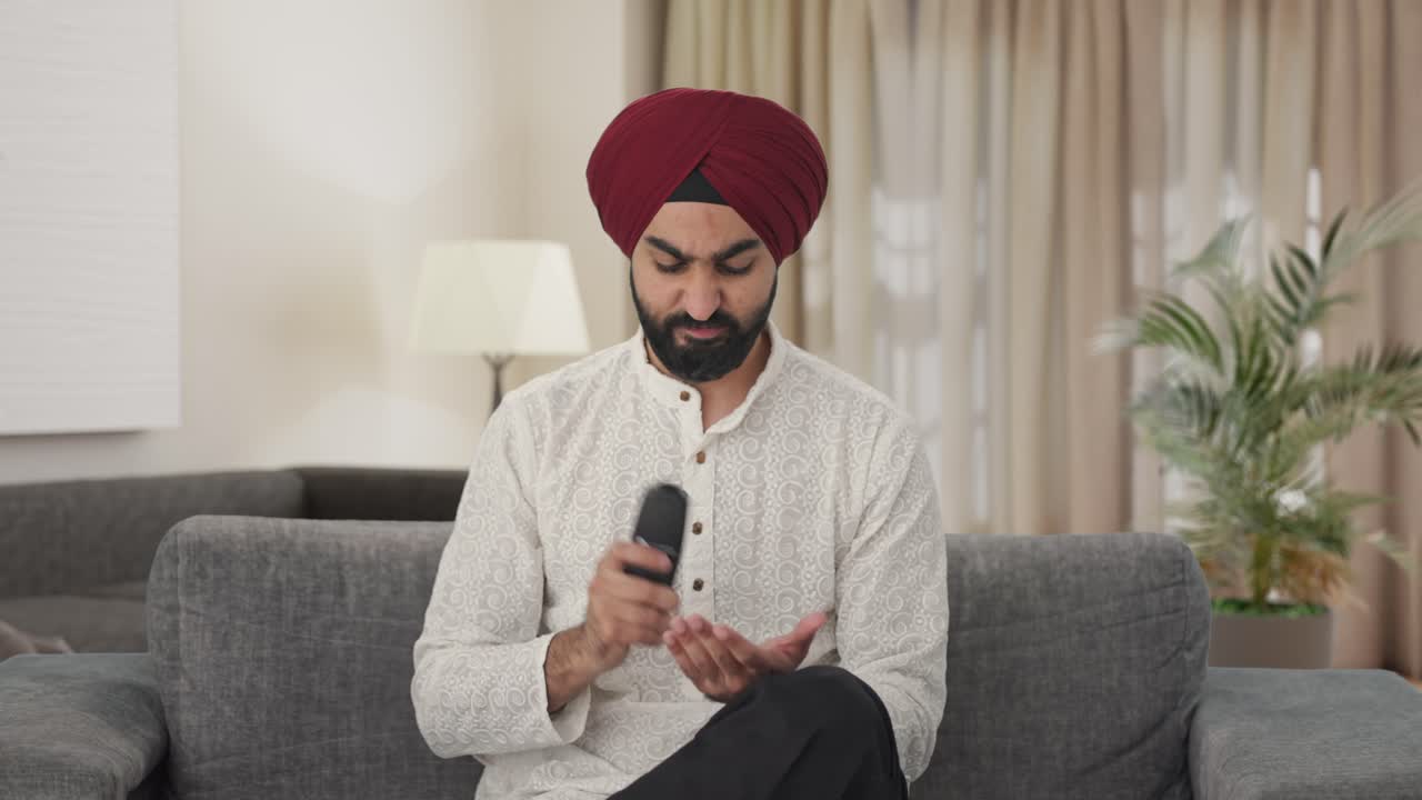 Uomo indiano Sikh frustrato che cerca di riparare il telecomando della TV.