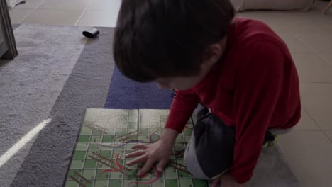 top view of caucasian boy , playing classic board game snakes and ladders on the carpet at living room indoors