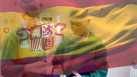 Animation-of-spain-flag-waving-over-diverse-surgeons-discussing-patients-reports-in-hospital