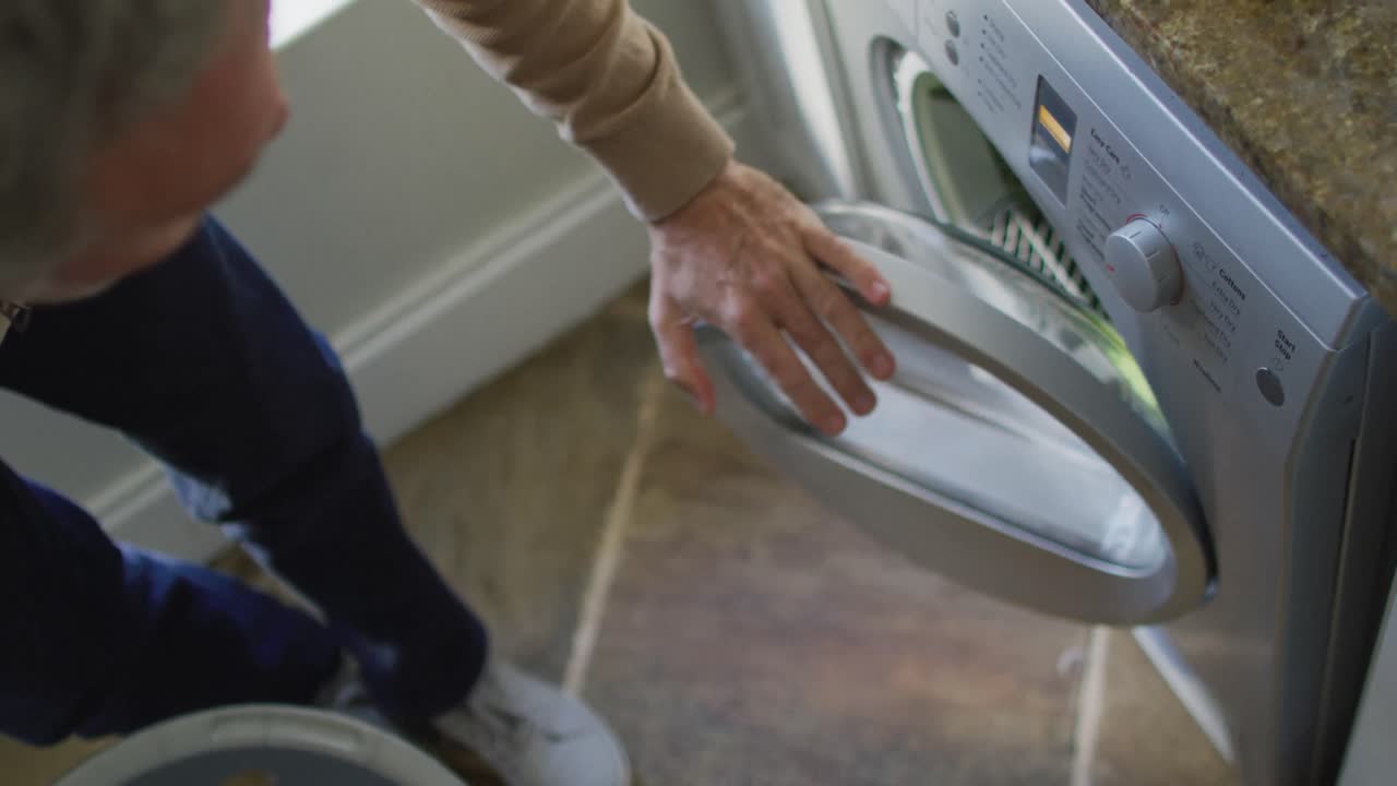 Happy caucasian man holding basket and doing laundry in kitchen