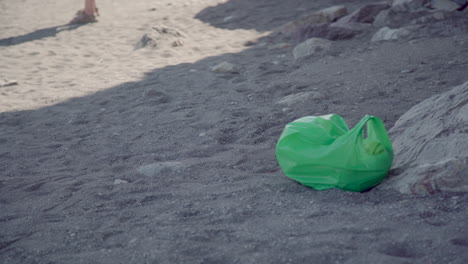 bolsa de plástico verde dejada como basura en la playa, contaminación por impacto humano