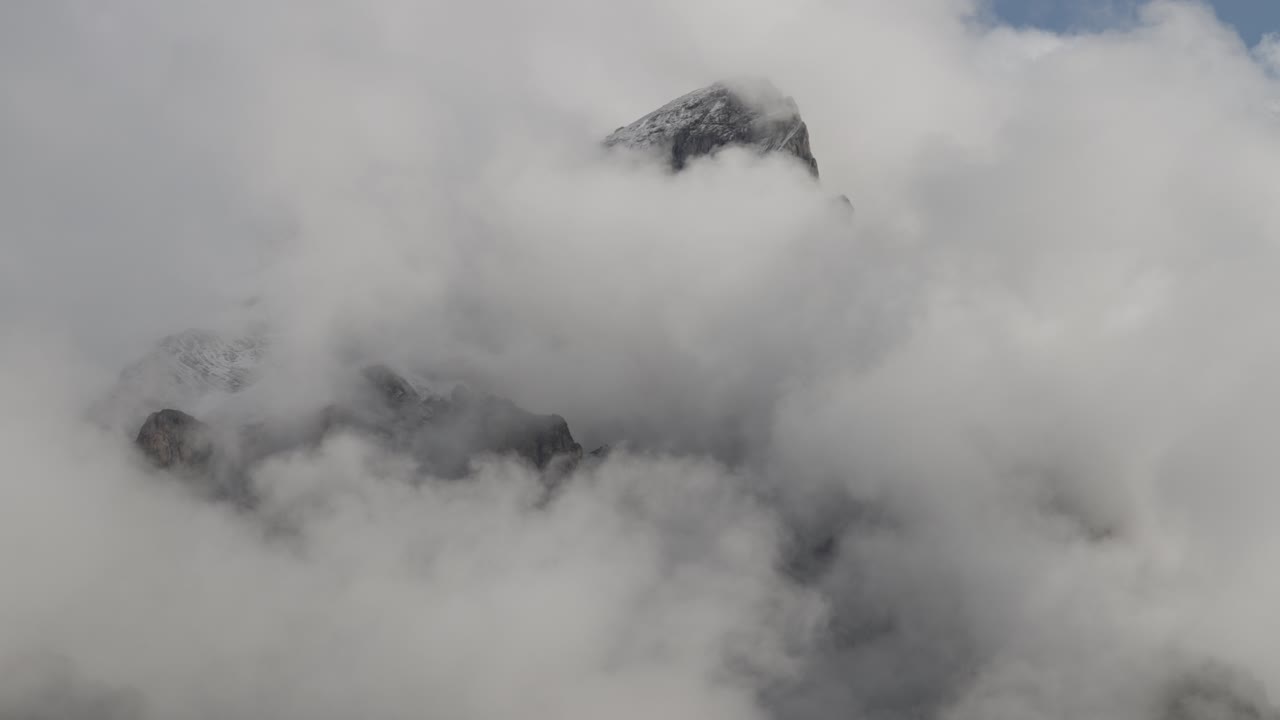 Mysterious mountain peak surrounded by moving clouds, summit in mist