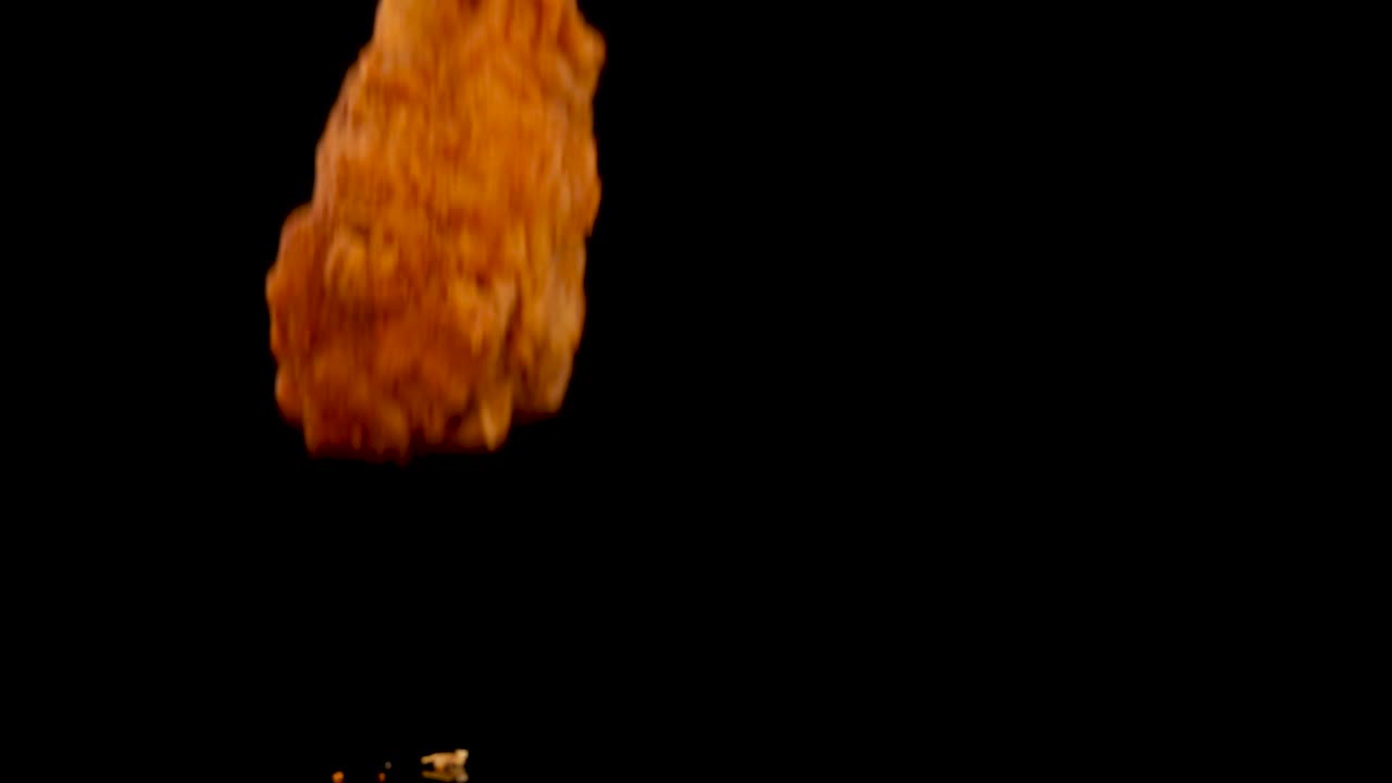 Golden fried chicken pieces fall and bounce on a glossy black background, scattering crumbs and spices. Dramatic lighting highlights texture and motion in slow motion