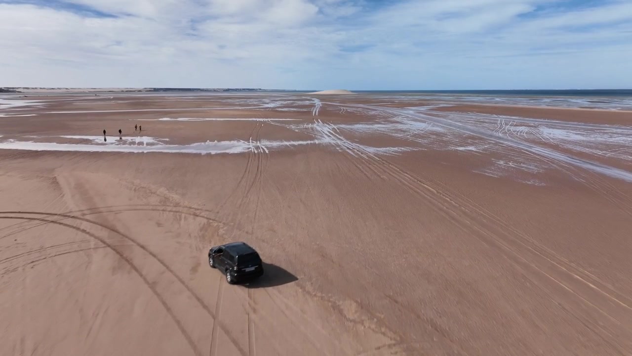 Vista aerea con drone delle tracce di veicoli che attraversano le vaste distese intertidali della Laguna di Dakhla, rivelando l'interazione tra l'attività umana e il dinamico paesaggio costiero lungo la costa atlantica del Marocco