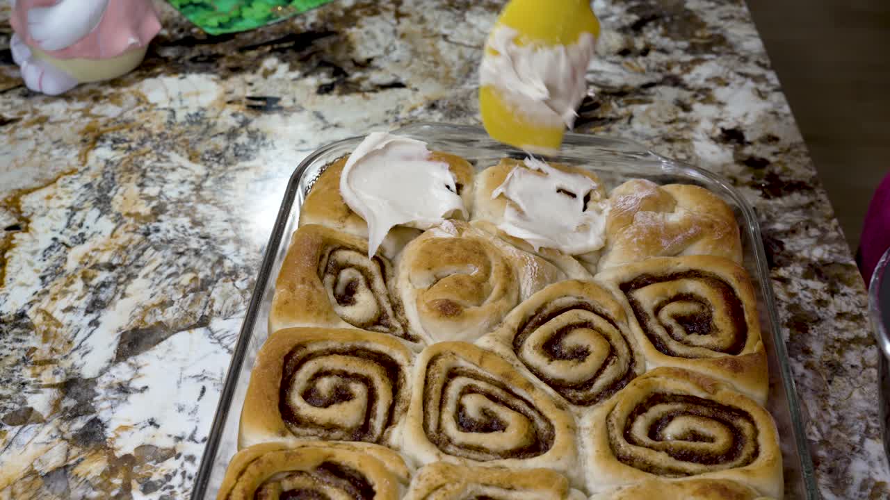 Icing homemade cinnamon rolls with cream cheese frosting