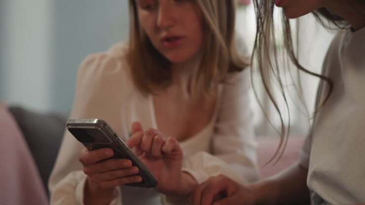Blonde woman shows baby photos to girlfriend on smartphone