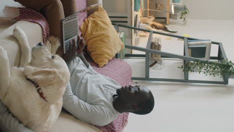 african american man using laptop and petting dog at home