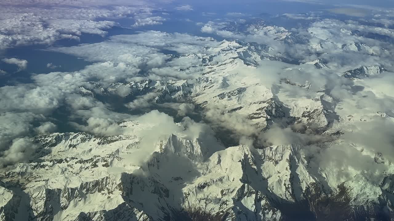 An aerial view of the Swiss Alps covered with snow, taken from a jet cockpit during a high altitude flight with the sunrise light.