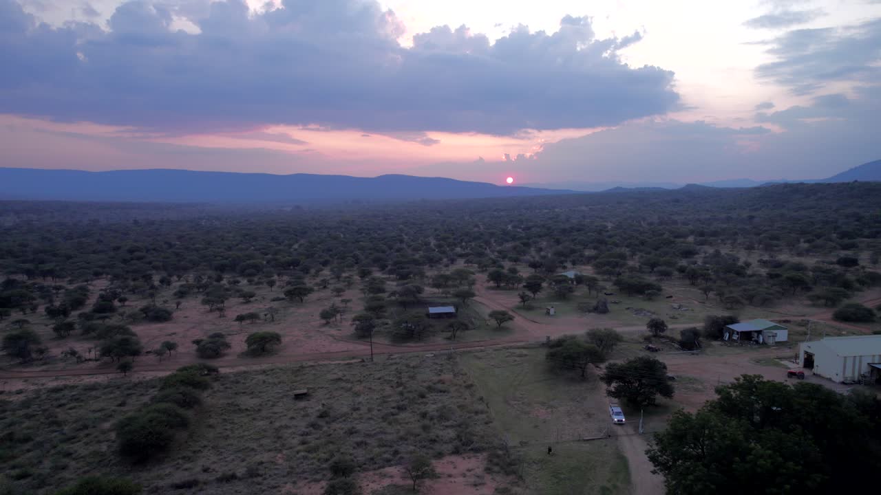Reverse aerial shot of African farms at sunset in South Africa, on a cloudy day as the sun disappears over the horizon.