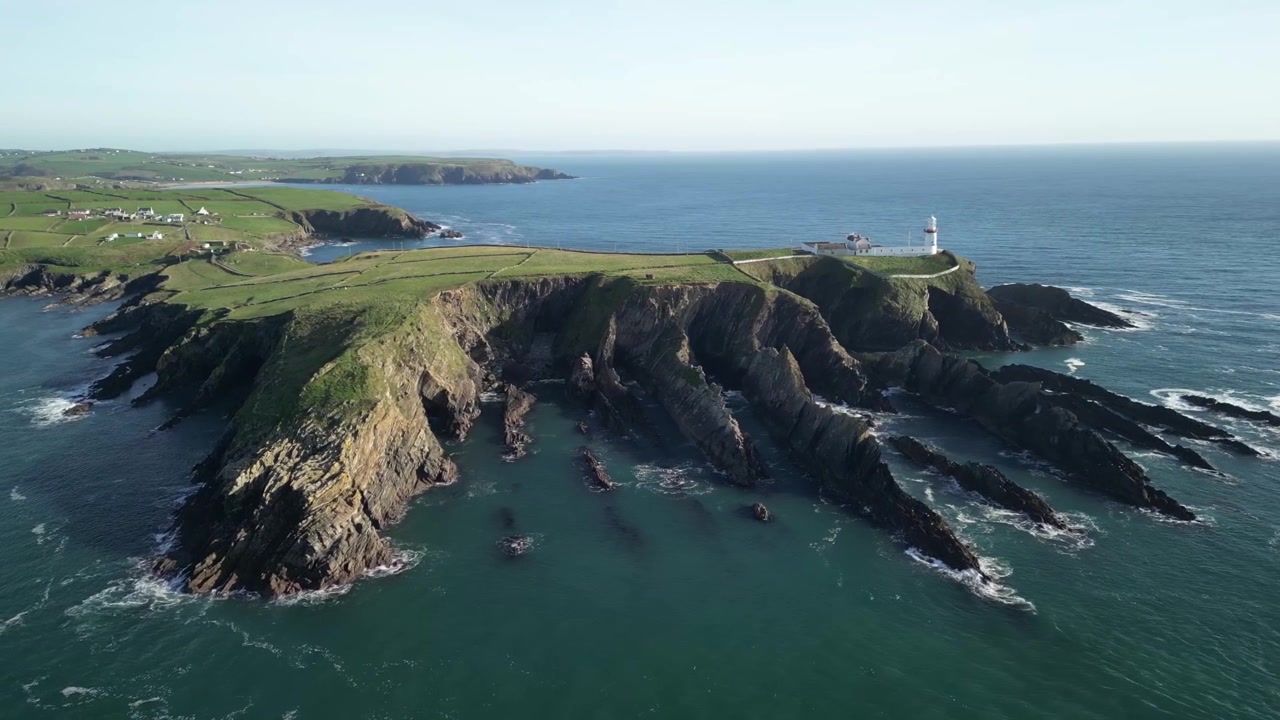 Drone svæver over spids odde med fyrtårn, Galley Head i West Cork, Irland. Stille Atlanterhav med bølger og klipper.