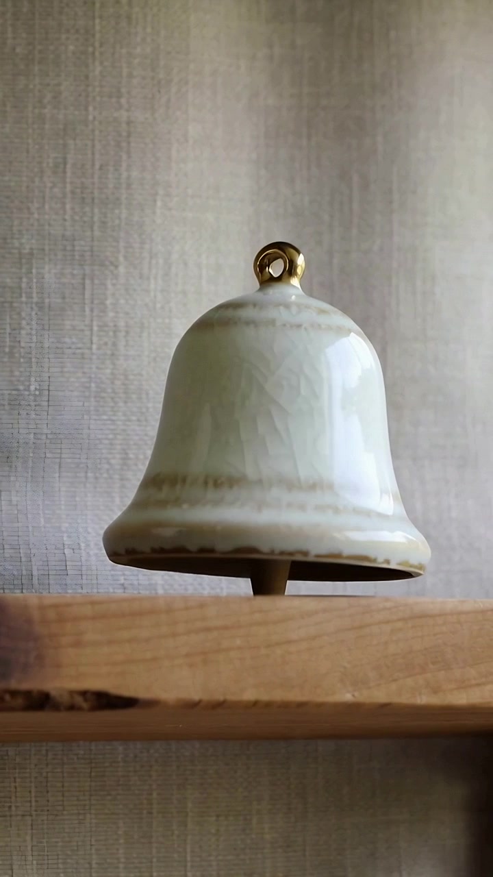 Vidéo verticale : Caméra en mouvement centrant une cloche en céramique, boucle dorée en rotation sur une étagère en bois, pot à gauche.
