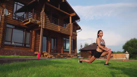 a slim and beautiful woman in sportswear with an open press is preparing to start training on the lawn near her home flexing her legs, knees, shins and thighs with warming up exercises