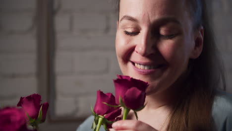 an attractive woman smells a bouquet of red roses and a smile appears on her face