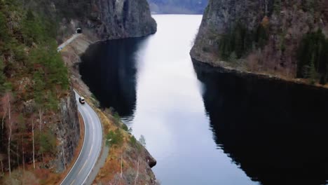 campervan drives along a winding road beside a tranquil fjord surrounded by rugged cliffs