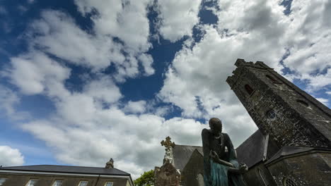 time lapse of 19th century famine statue and medieval church in rural ireland with passing clouds and sunshine