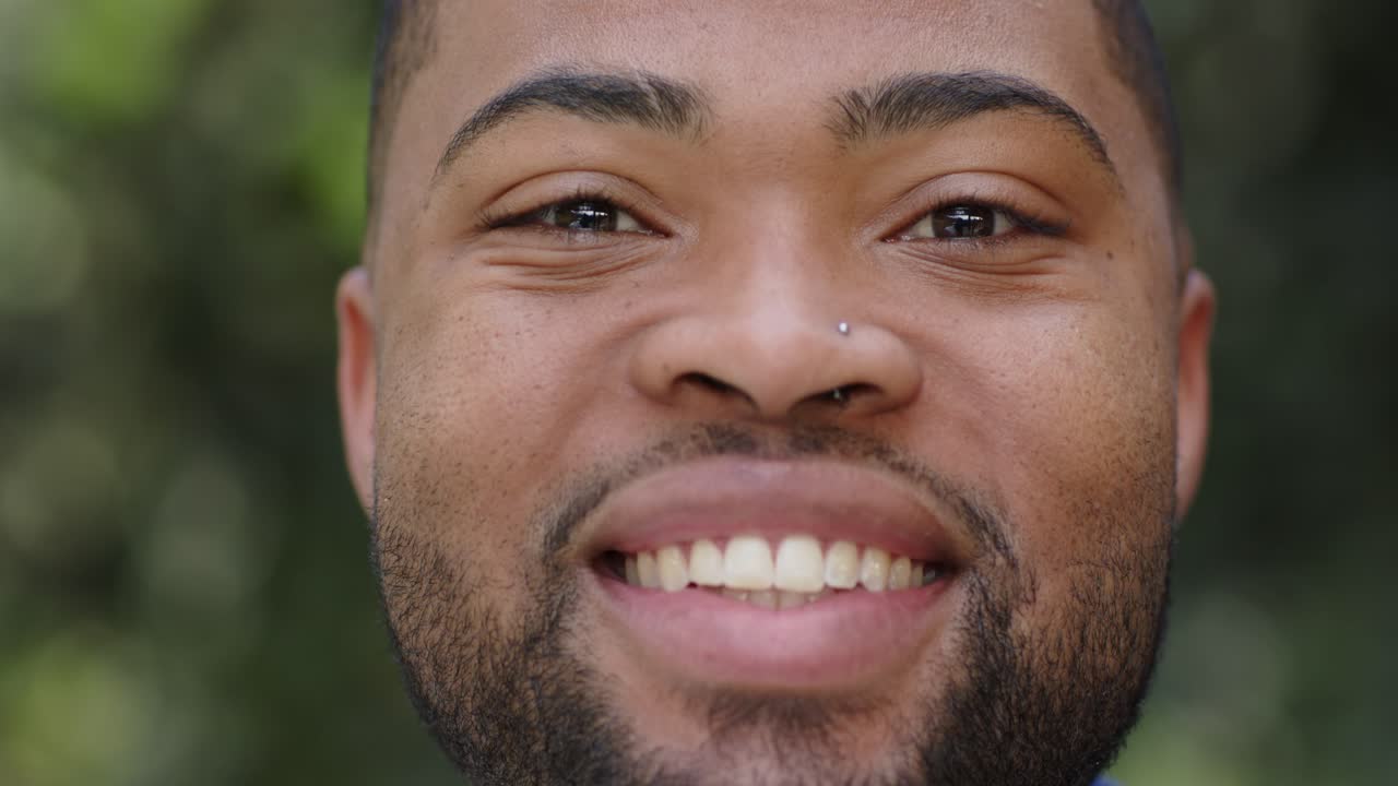 Receiving camera focus, African American man forming smile, laughing outdoors with silver nose stud