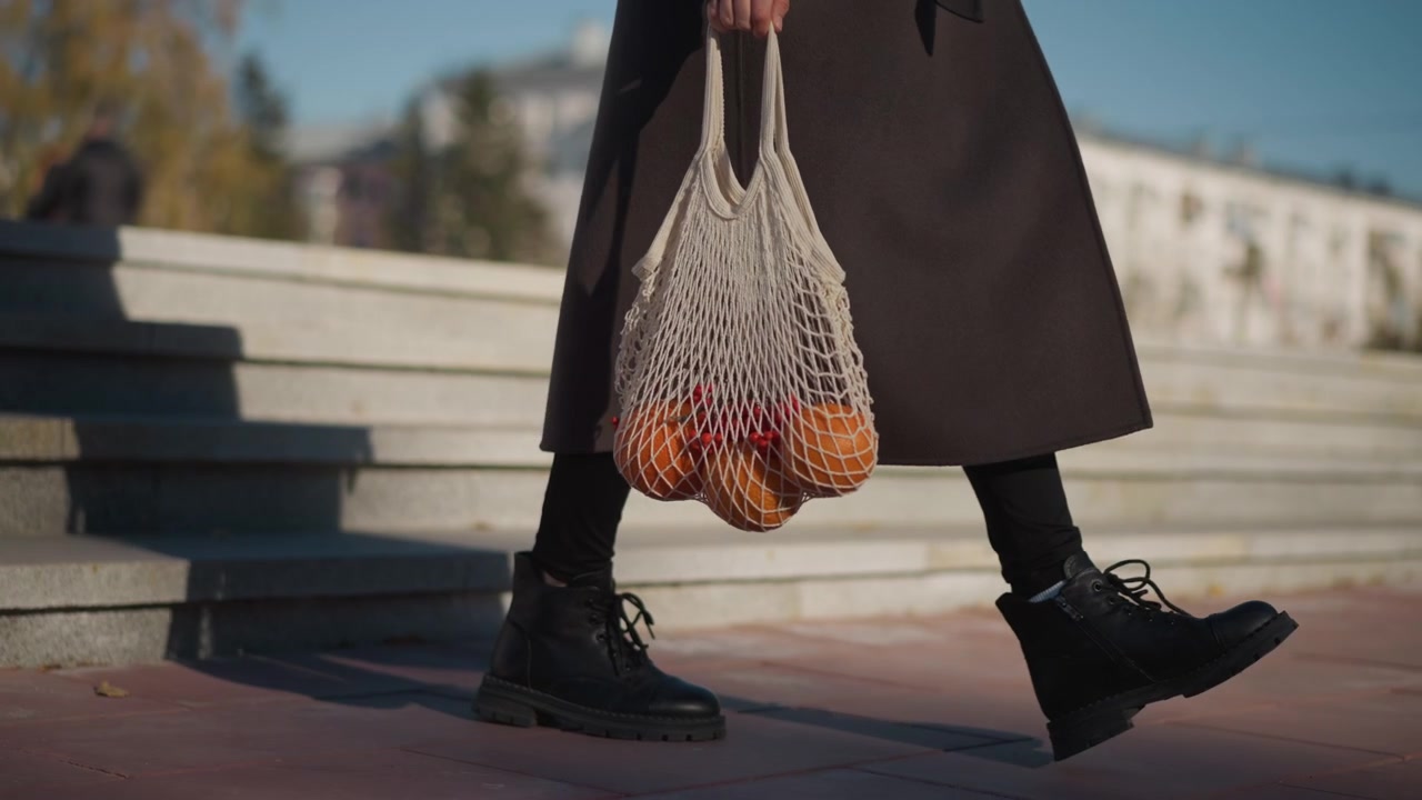 Donna che scende le scale della città portando una borsa a rete di arance.