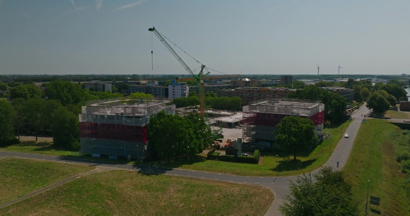 Un dron se acerca a una obra de construcción holandesa con grúas y nuevos edificios de apartamentos en una zona residencial, destacando el desarrollo de viviendas, el crecimiento económico y la expansión urbana.