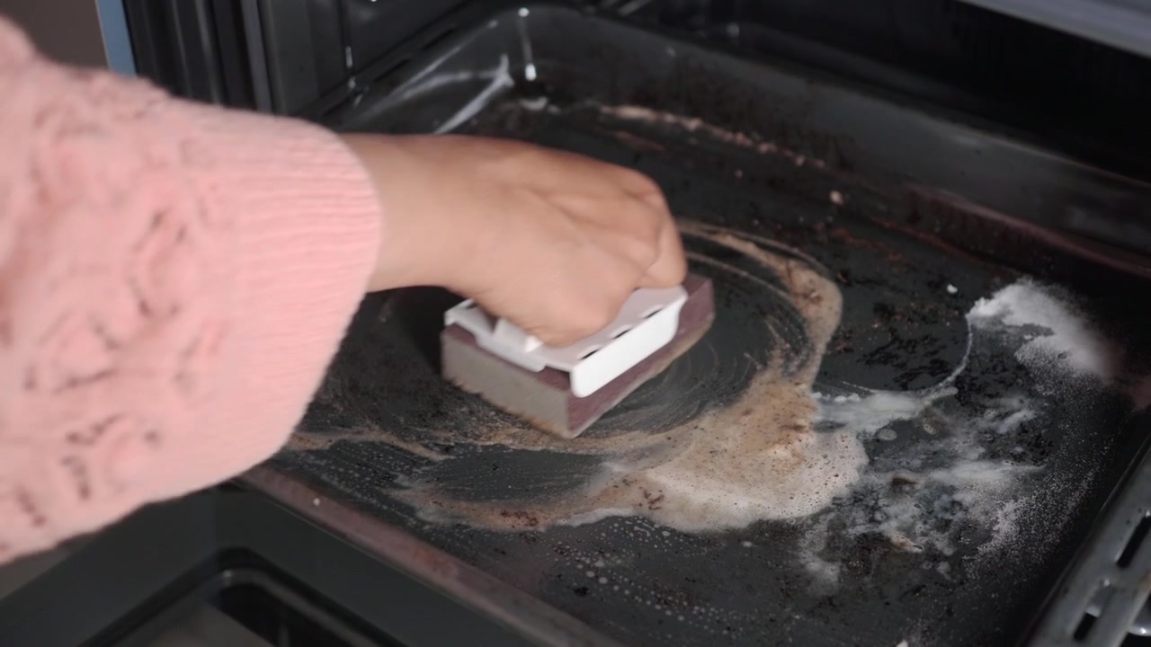 Person Scrubbing Dirty Oven Tray with Sponge