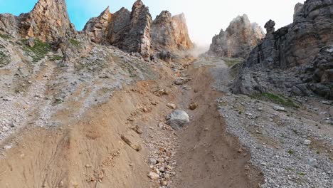 Drone-ascent-towards-misty-Dolomite-rock-pillars,-revealing-rugged-paths-and-the-promise-of-towering-formations-up-close