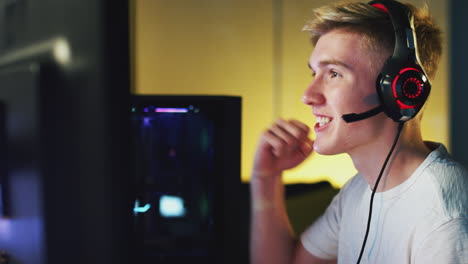adolescente emocionado que usa auriculares ganando en el juego en casa usando dos pantallas de computadora