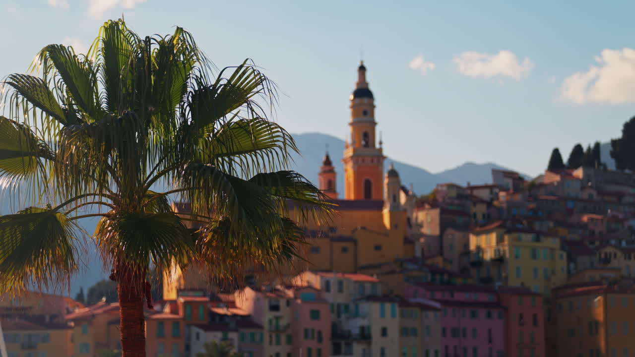 Distant view of the St Michel Basilica surrounded by colourful buildings and palm trees, Menton, France