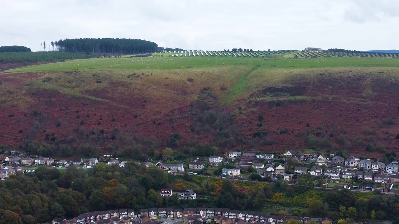 Vista aerea discendente con drone di una fattoria di pannelli solari su una collina con case alimentate da energia rinnovabile sottostante. Concetto di energia pulita naturale 4K.