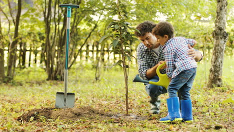 Portrait of a boy and his dad planting a tree. They water the tree. Dad helps his son. Blurred background
