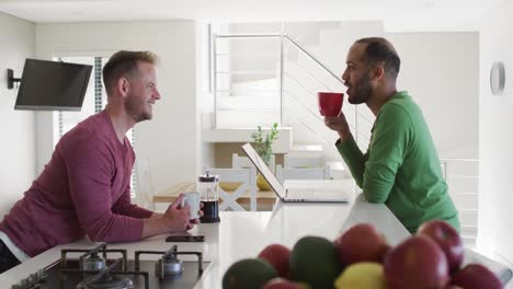multi ethnic gay male couple drinking coffee talking in kitchen