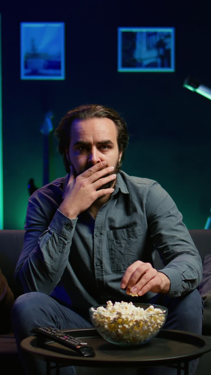 Vertical video Man watching suspenseful thriller film, eating popcorn, close up