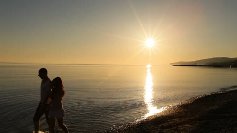 Couple walking on water at sunset. Silhouette of young couple walking by the hand on water at sunset