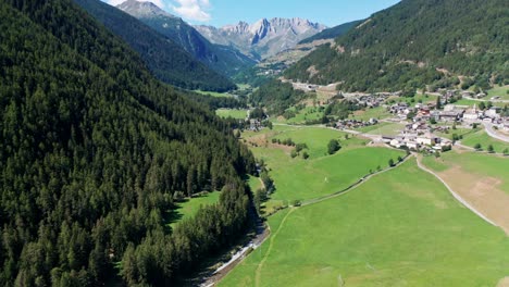 green valley between huge mountain ranges with fields and a small village under a blue sky, drone panoramic view