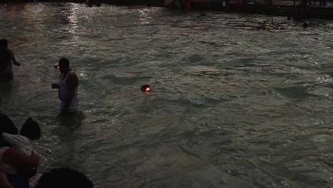 Earthen light lamps and people bathing on the banks of the Ganges river in Haridwar, slow motion shot.