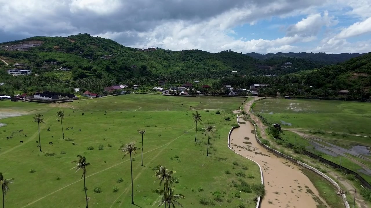 Vista cinematográfica de drone da Praia de Areguling, Lombok, na estação chuvosa. Falésias verdes exuberantes contrastam com o oceano com tons marrons do rio, exibindo uma dramática costa tropical e montanhas.
