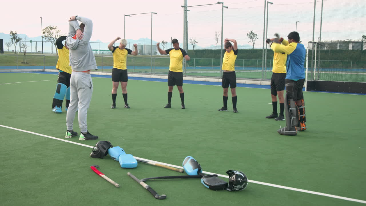male hockey team stretching on field with coach, preparing for practice session