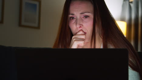 anxious woman sitting on sofa at home at night looking at laptop concerned about social media or bad news 4