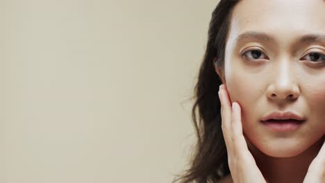 Asiatische-Frau-Mit-Dunklem-Haar,-Die-Ihr-Gesicht-Auf-Beigem-Hintergrund-Mit-Kopierraum-Berührt,-Zeitlupe