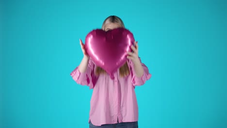 Blonde-Frau,-Die-Einen-Herzförmigen-Lila-Ballon-Umarmt,-Valentinstagstimmung-Mit-Blauem-Hintergrund