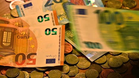 a various set of euro bills fluttering onto a table covered in euro coins , close up shot