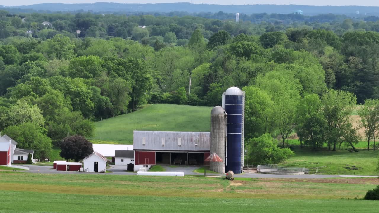 Aerial zoom shot of american farmstead with red barn, silo storage and house in front of green forest landscape. Dairy and fields in rural area. Pennsylvania, USA. Panorama