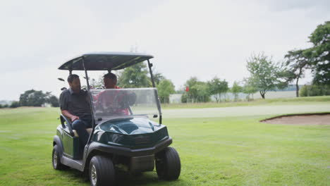 two male golfers driving golf buggy along course to green