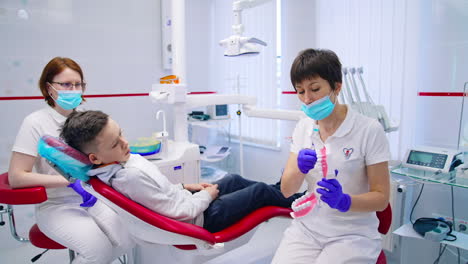 Teenage boy attending dentist's office. Female doctor explaining the kid rules of correct teeth brushing.